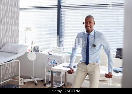 Portrait von lächelnden männlicher Arzt mit Stethoskop stehen Schreibtisch im Büro Stockfoto