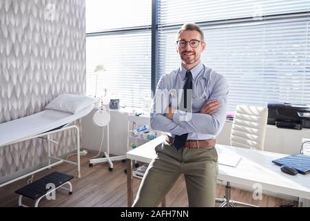 Portrait von lächelnden Reife männlicher Arzt mit Stethoskop stehen Schreibtisch im Büro Stockfoto