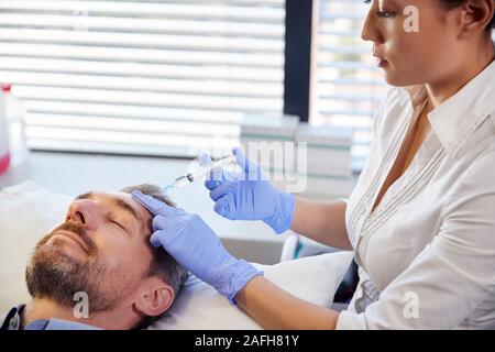 Weibliche Kosmetikerin Geben ältere männliche Patienten Botox Injektion in die Stirn Stockfoto