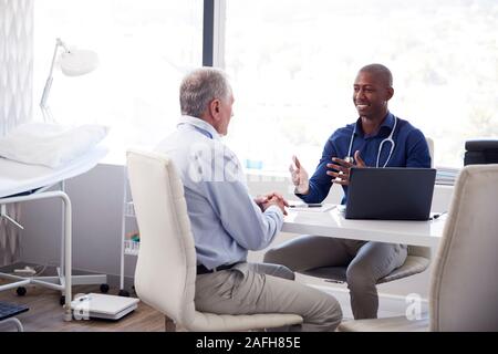 Ältere männliche Patienten in Absprache mit dem Arzt Sitzen am Schreibtisch im Büro Stockfoto