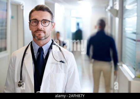 Portrait von ausgewachsenen männlichen Arzt tragen weiße Mantel mit Stethoskop in Langen Krankenhaus Flur Stockfoto