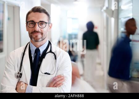 Portrait von ausgewachsenen männlichen Arzt tragen weiße Mantel mit Stethoskop in Langen Krankenhaus Flur Stockfoto