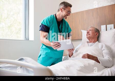 Chirurg mit digitalen Tablet Besuchen ältere männliche Patienten im Krankenhausbett in Geriatrische Einheit Stockfoto