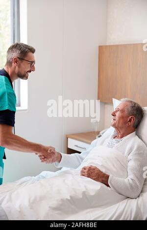 Chirurg besuchen und das Händeschütteln mit älteren männlichen Patienten im Krankenhausbett in Geriatrische Einheit Stockfoto