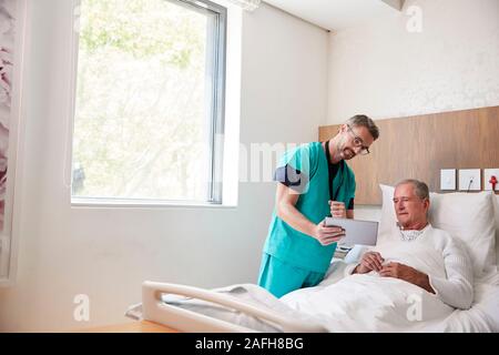 Chirurg mit digitalen Tablet Besuchen ältere männliche Patienten im Krankenhausbett in Geriatrische Einheit Stockfoto