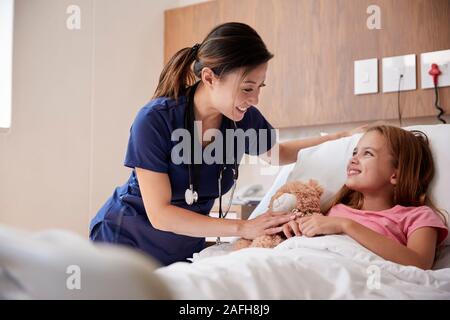 Weibliche Krankenschwester besuchen Mädchen liegt im Krankenhaus Bett umarmen Teddybär Stockfoto