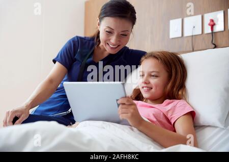 Weibliche Krankenschwester mit Mädchen liegt im Krankenhaus Bett Blick auf Digitale Tablet zusammen Stockfoto