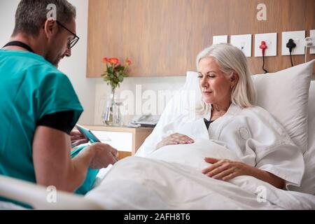 Chirurg mit digitalen Tablet besuchen und das Gespräch mit Reife Weibliche Patienten im Krankenhaus Bed Stockfoto