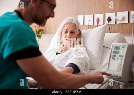 Männliche Krankenschwester unter reife weibliche Patienten Blutdruck im Krankenhausbett mit automatisierten Maschine Stockfoto