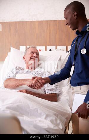 Arzt Händeschütteln mit älteren männlichen Patienten im Krankenhausbett in Geriatrische Einheit Stockfoto