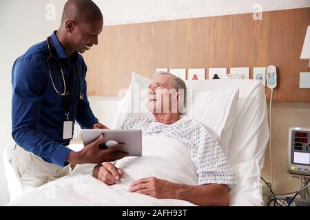 Arzt mit digitalen Tablet besuchen und das Gespräch mit älteren männlichen Patienten im Krankenhaus Bed Stockfoto