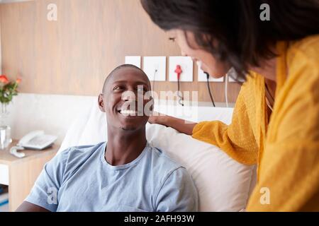 Frau besuchen und im Gespräch mit Patienten Mann im Krankenhaus Bed Stockfoto
