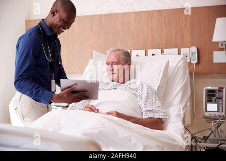 Arzt mit digitalen Tablet besuchen und das Gespräch mit älteren männlichen Patienten im Krankenhaus Bed Stockfoto