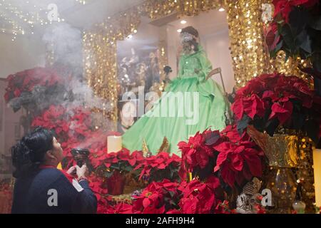 Ein Santa Muerte devotee betet an einem Tempel in Jackson Heights, Queens, New York City. Sie bläst Rauch bei einer Gottheit als benutzerdefiniert ist. Stockfoto