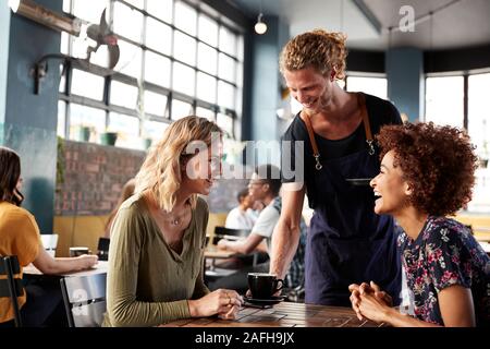 Zwei weibliche Freunde am Tisch sitzen in Coffee Shop serviert der Kellner Stockfoto