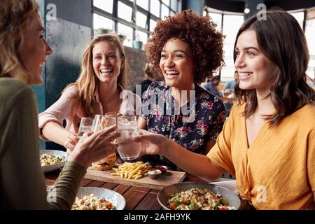 Vier junge weibliche Freunde treffen für die Getränke und das Essen einen Toast im Restaurant Stockfoto