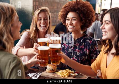 Vier junge weibliche Freunde treffen für die Getränke und das Essen einen Toast im Restaurant Stockfoto