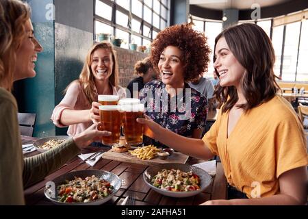 Vier junge weibliche Freunde treffen für die Getränke und das Essen einen Toast im Restaurant Stockfoto