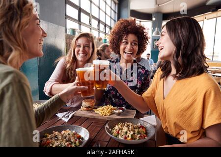 Vier junge weibliche Freunde treffen für die Getränke und das Essen einen Toast im Restaurant Stockfoto