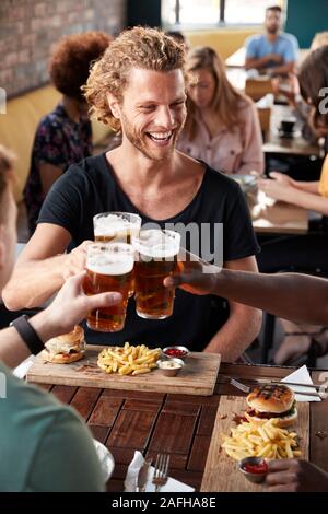 Drei junge männliche Freunde treffen für die Getränke und das Essen einen Toast im Restaurant Stockfoto
