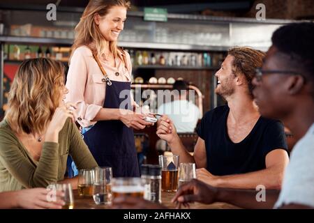 Kellnerin hält Kreditkarte Maschine als Kunde zahlt Rechnung in Bar Restaurant Stockfoto