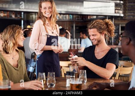 Kellnerin hält Kreditkarte Maschine als Kunde zahlt Rechnung in Bar Restaurant Stockfoto