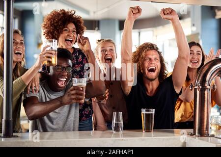 Gruppe von männlichen und weiblichen Freunde feiern, während gerade Spiel auf dem Bildschirm In der Sports Bar Stockfoto