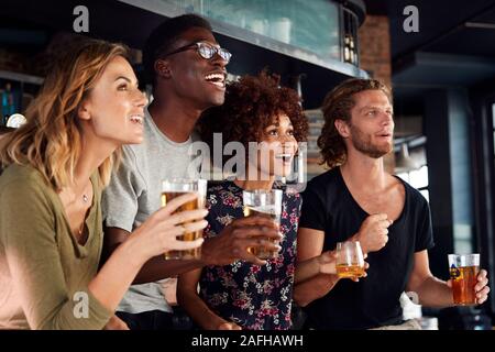 Gruppe von männlichen und weiblichen Freunde feiern, während gerade Spiel auf dem Bildschirm In der Sports Bar Stockfoto