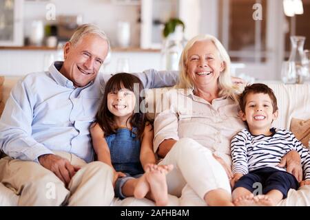 Weiß älterer Paare und ihre Enkelkinder auf einem Sofa zusammen zu Hause sitzt lächelnd in die Kamera Stockfoto