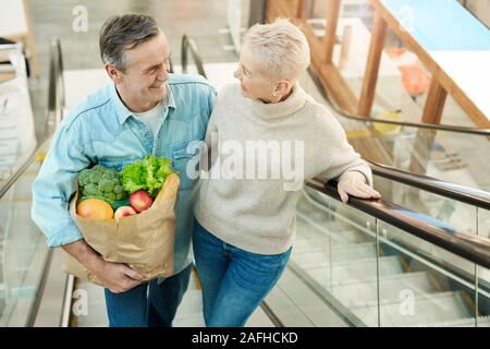 Hohen winkel Porträt des modernen senior Paar, Rolltreppe und Holding grocery bag während triefend in der Mall, kopieren Raum Stockfoto