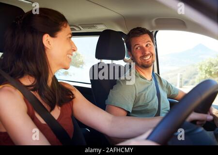 Mitte der Erwachsenen weiß Frau fahren Auto, zu ihrem Mann auf dem Beifahrersitz lächelnd, Seitenansicht Stockfoto