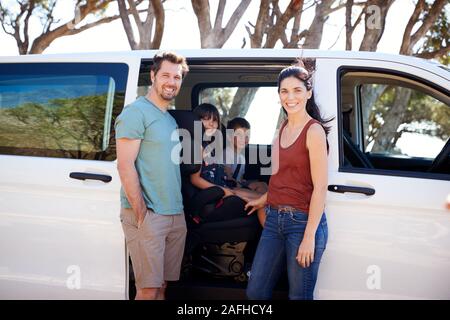 Mitte nach weißen Eltern stand neben dem Auto, ihre zwei jungen Kinder Lächeln für die Kamera Stockfoto
