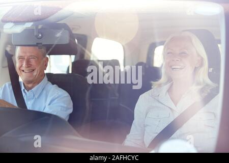 Senior weiß Paar fahren in ihr Auto an einem sonnigen Tag, durch die vordere Windschutzscheibe Stockfoto