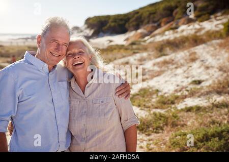 Senior weiß Paar stehend auf einem Strand umarmen und lächelnd in die Kamera, in der Nähe Stockfoto