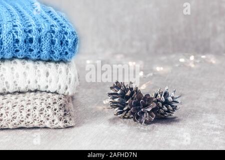 Stilvolle gestrickt, pastellfarbenen Pullover und eine in der Trendfarbe Blau im Stapel mit Tannenzapfen und Weihnachtslichter auf Samtigen Stoff Hintergrund gefaltet Stockfoto