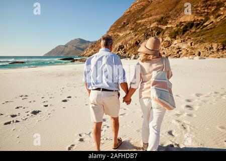 Senior weiß Paar am Strand halten sich an den Händen, Blick nach hinten, drei Viertel Länge, in der Nähe Stockfoto