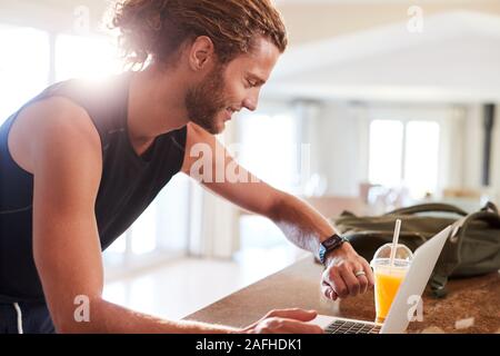 Tausendjährige weiße Mann Kontrolle fitness App auf Beobachten und Laptop nach einem Workout, Seitenansicht Stockfoto