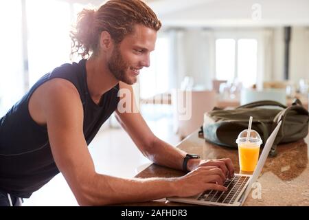 Tausendjährige weiße Mann Kontrolle fitness App auf Laptop zu Hause nach dem Training, Seitenansicht Stockfoto