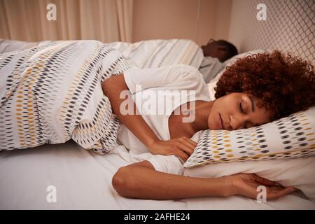 Tausendjährige afrikanische amerikanische Frau an Ihrer Seite schlafend im Bett liegend, Ihr Partner im Hintergrund Stockfoto