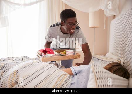 Mixed Race Paar feiern, Mann seinen Partner Frühstück und Geschenke in Bett bringen, in der Nähe Stockfoto