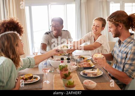 Zwei junge Frauen, die ein Gericht über den Tisch beim Essen mit Freunden, in der Nähe Stockfoto