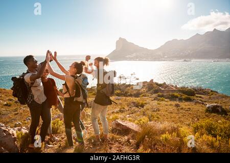 Junge Erwachsene mit Freunden auf einer Wanderung feiern zu einem Gipfel in der Nähe der Küste, volle Länge, Seitenansicht Stockfoto