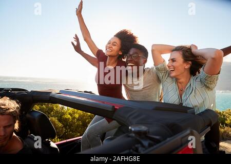 Aufgeregt tausendjährigen Freunde in einem offenen Wagen Reisen mit den Armen in der Luft Stockfoto