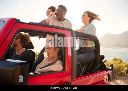 Fünf junge erwachsene Freunde auf einer Autofahrt in einem oben offenen Jeep durch das Meer Stockfoto