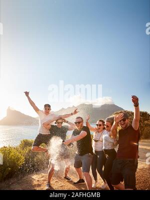 Sechs junge erwachsene Freunde feiern auf einem küstenweg Eine Flasche Champagner öffnen Stockfoto