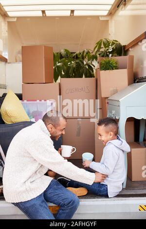 Vater und Sohn sitzen auf Heckklappe Ausbau Lkw mit Drink am Umzugstag Stockfoto