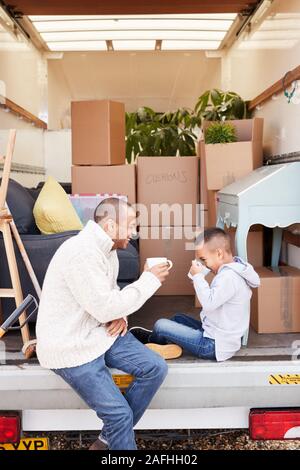 Vater und Sohn sitzen auf Heckklappe Ausbau Lkw mit Drink am Umzugstag Stockfoto