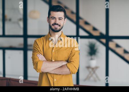 Foto von hübscher Kerl mit gekreuzten Händen stehen in modernen Apartments im Innenbereich machen Büro für Unternehmen Mitglieder neu erstellen Stockfoto
