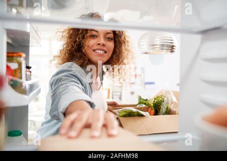 Blick aus dem Inneren des Kühlschranks als Frau entpackt Online Home Food Delivery Suchen Stockfoto