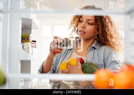 Anzeigen, die von der Innenseite der Kühlschrank als Frau öffnet Tür und Packs Essen auf Regalen Stockfoto